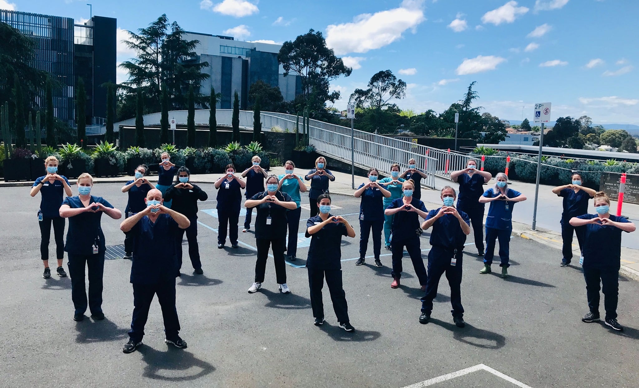 A group of Austin Health staff members wearing masks stand near the pedestrian footbridge over Burgundy Street, Heidelberg.